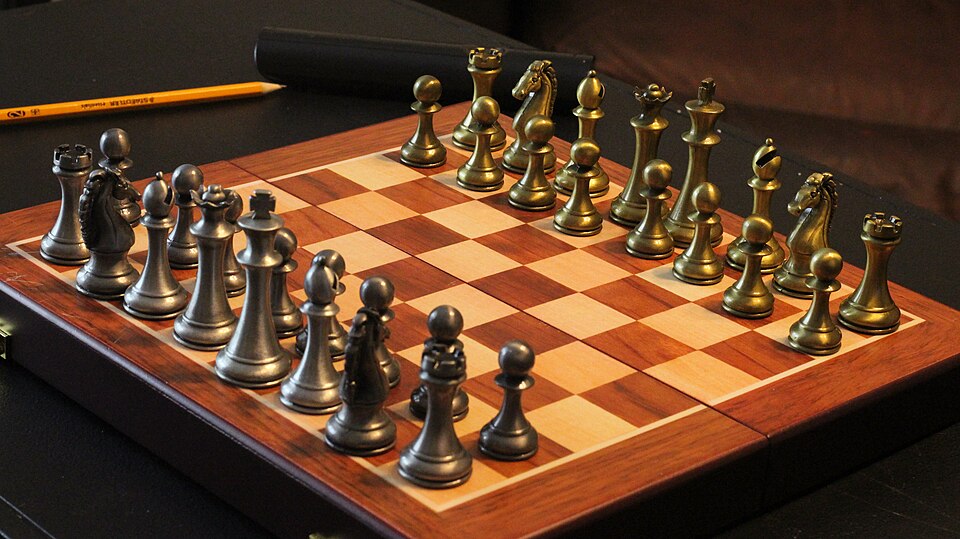 Gold and dark silver metal chess pieces lined up on a wood-grain board