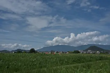 青空と白い雲の下に山並みと田園風景が広がる