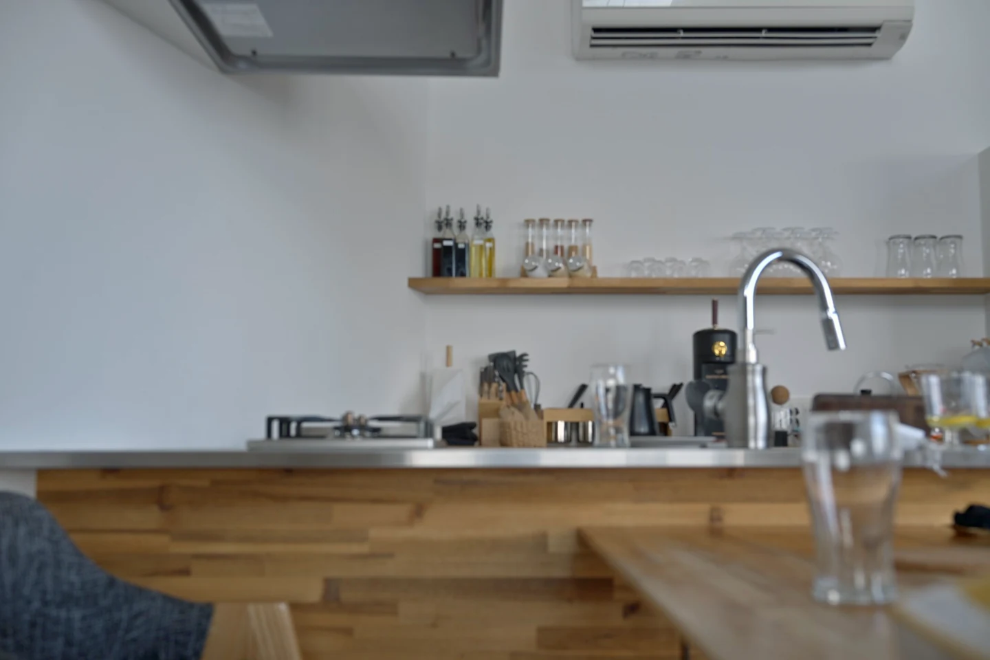 テーブルから見たカウンターキッチン。棚にグラスや瓶が並び、手前に調理器具と水栓がある