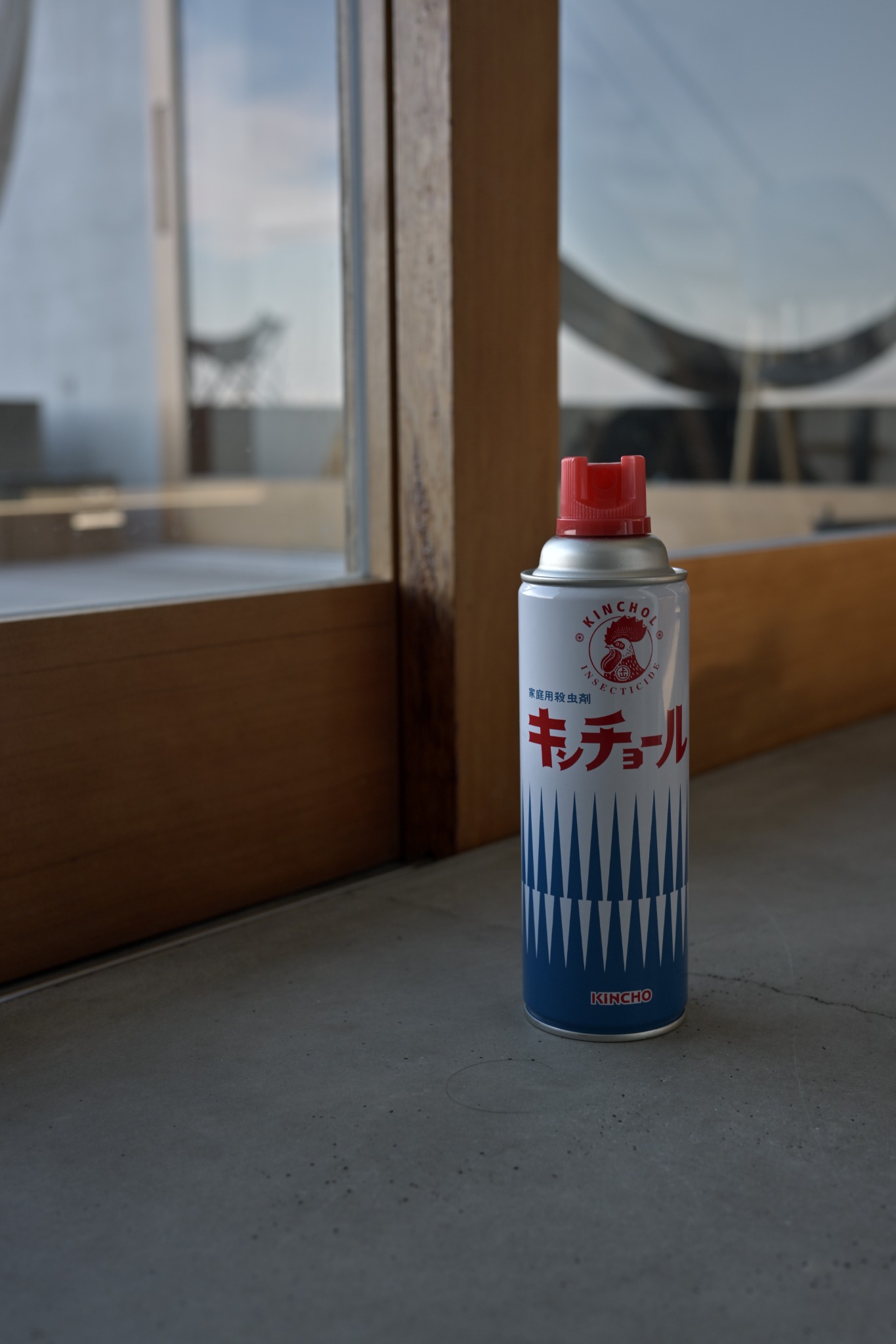 木枠の窓のそばに置かれた、赤い噴射口と白・青の缶のキンチョール