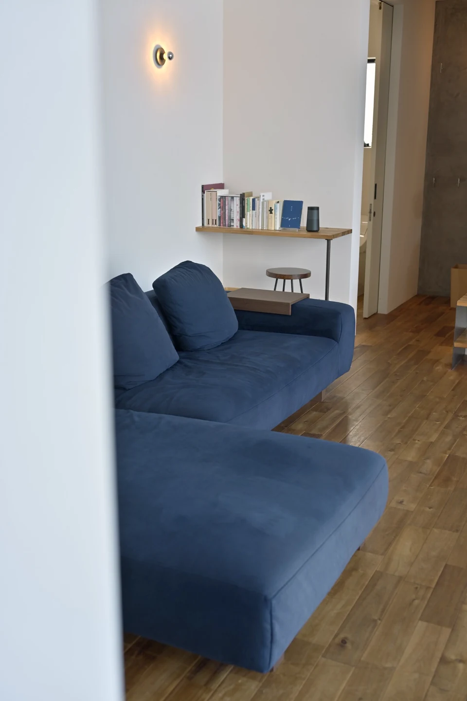 木の床のリビングに置かれた青いソファと、本が並んだ壁の棚