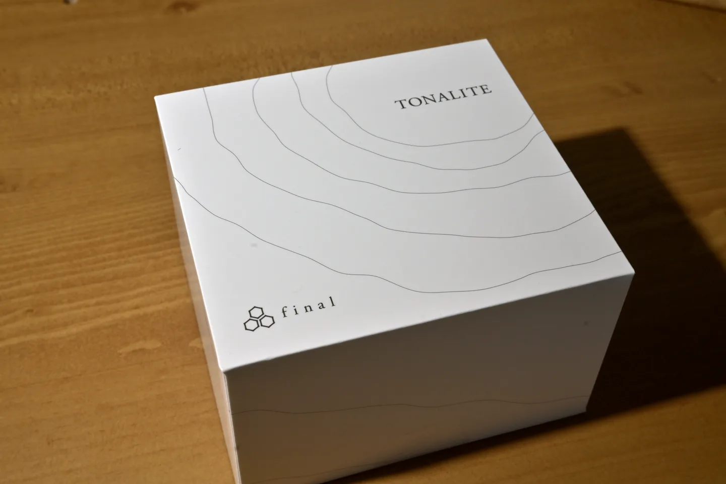 等高線のような細い線とTONALITEの文字、finalのロゴが入った白い箱