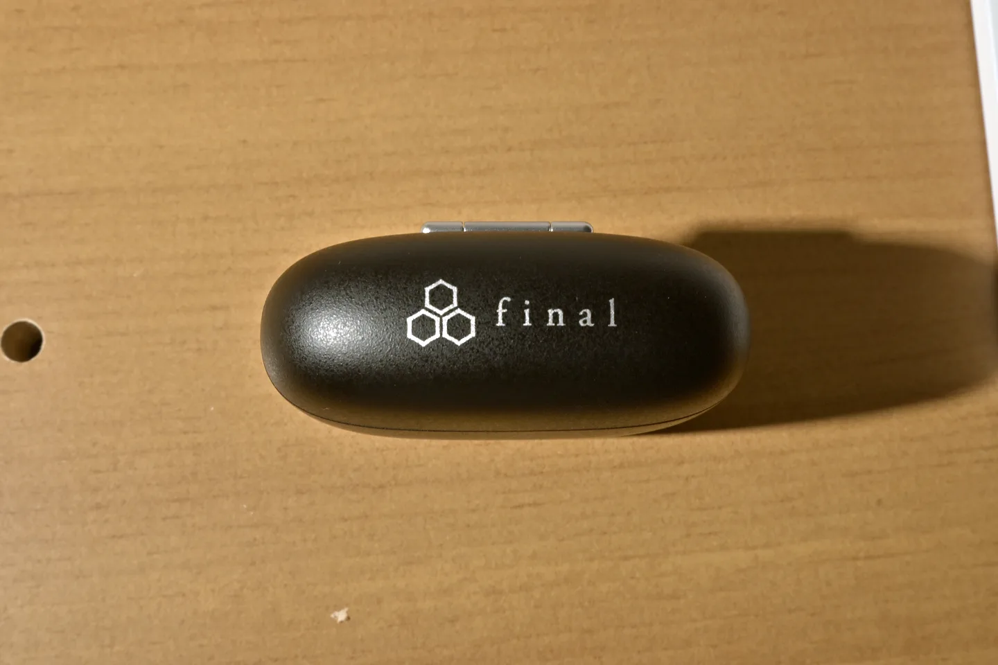 木の机の上に置かれた、白いfinalのロゴが入った黒い楕円形の充電ケース